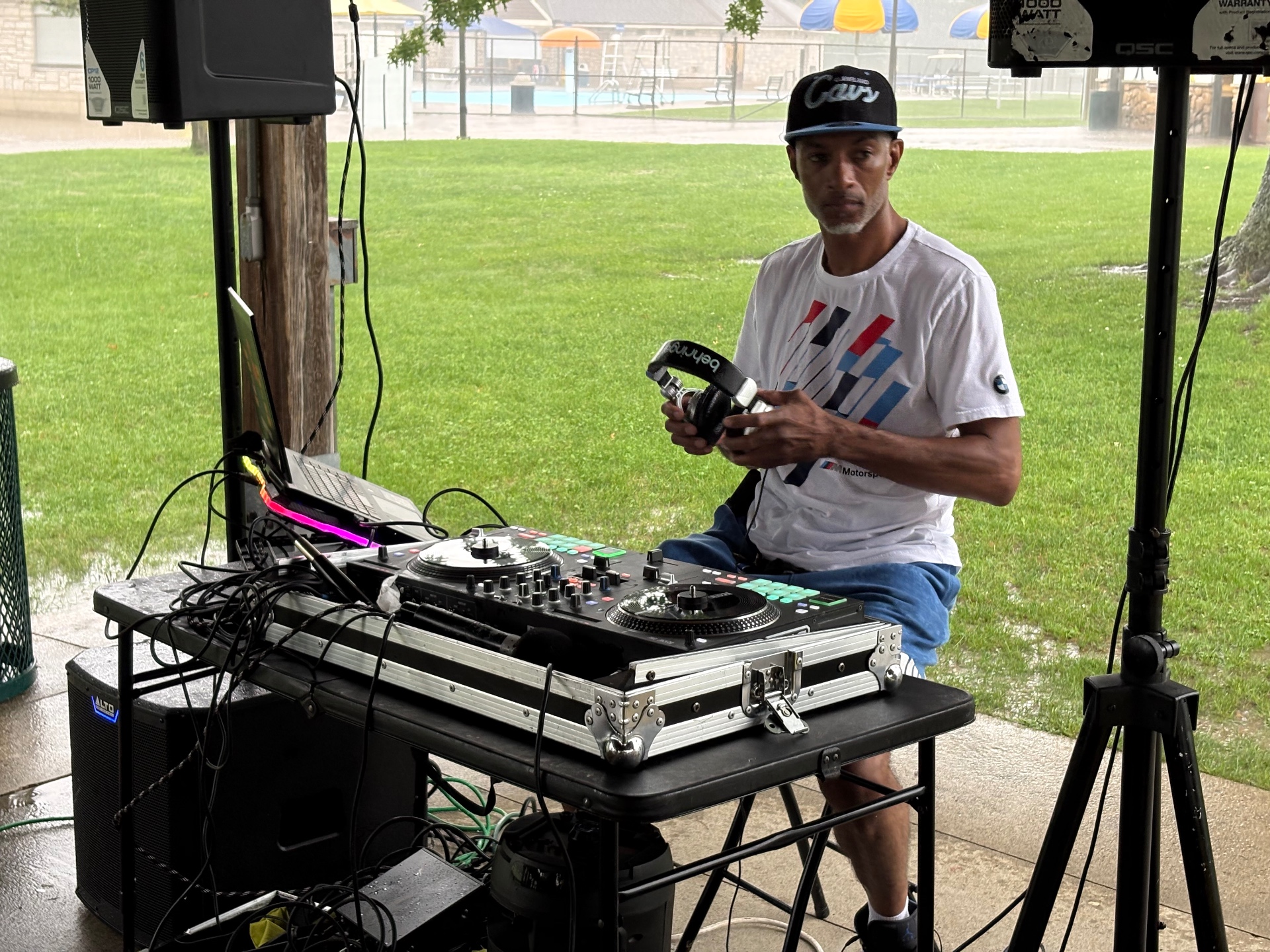 A DJ in a Cleveland Cavs cap holding headphones behind his turntables at the Push Me Dad park celebration
