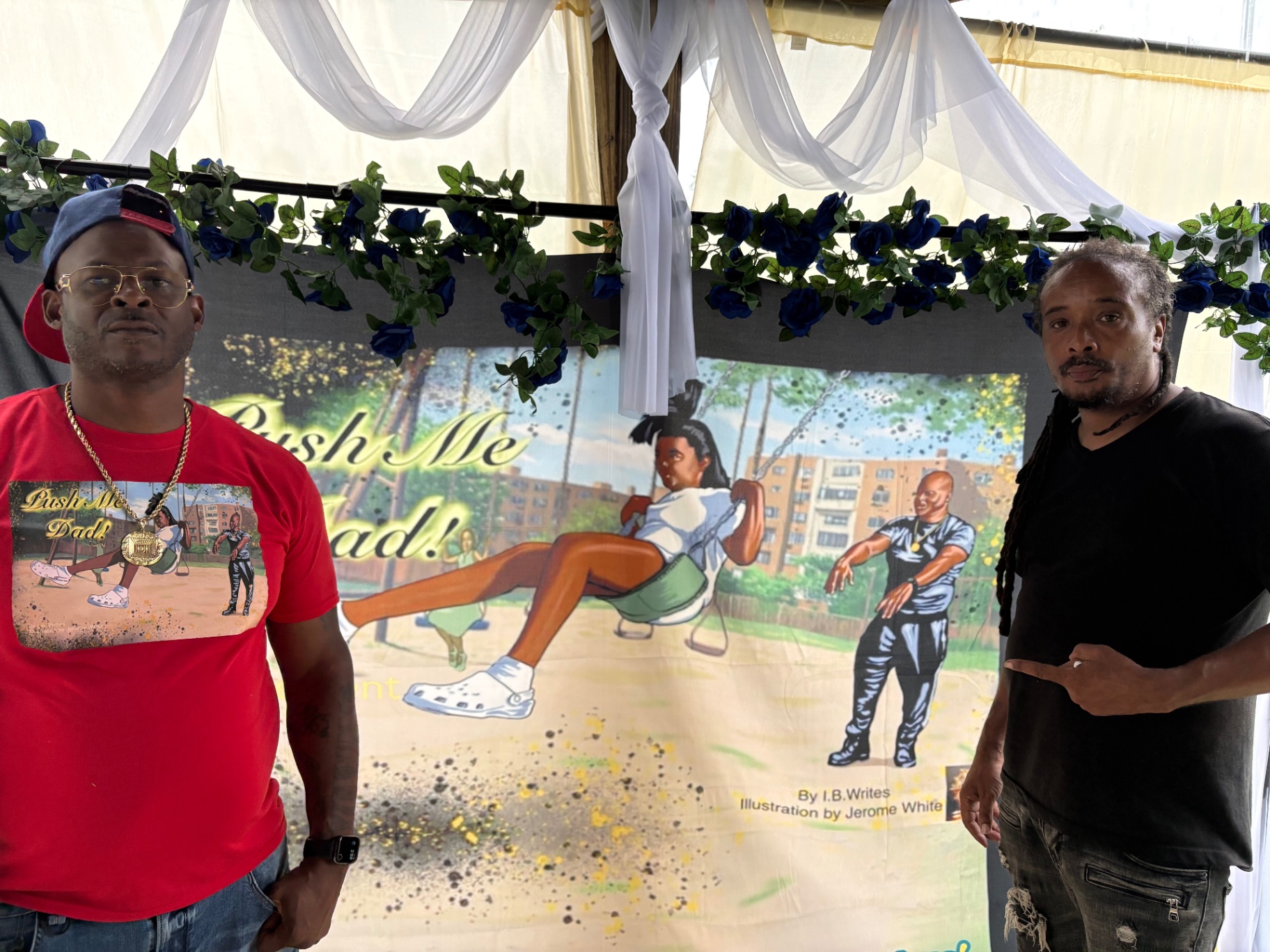 Two Black men posing on either side of the Push Me Dad book banner, one pointing at the cover art