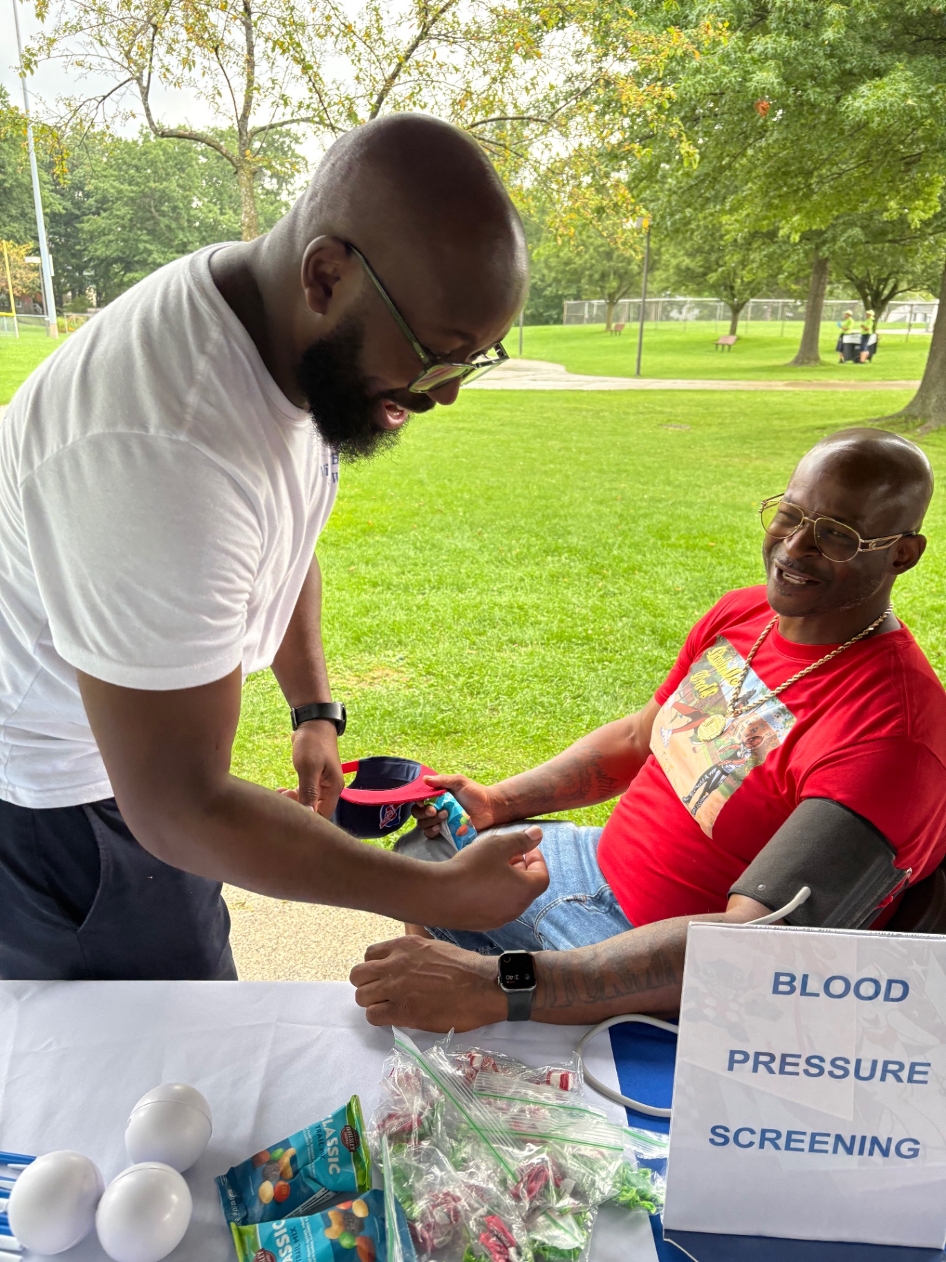 A health volunteer laughing with a father during his blood pressure check at the Push Me Dad wellness table