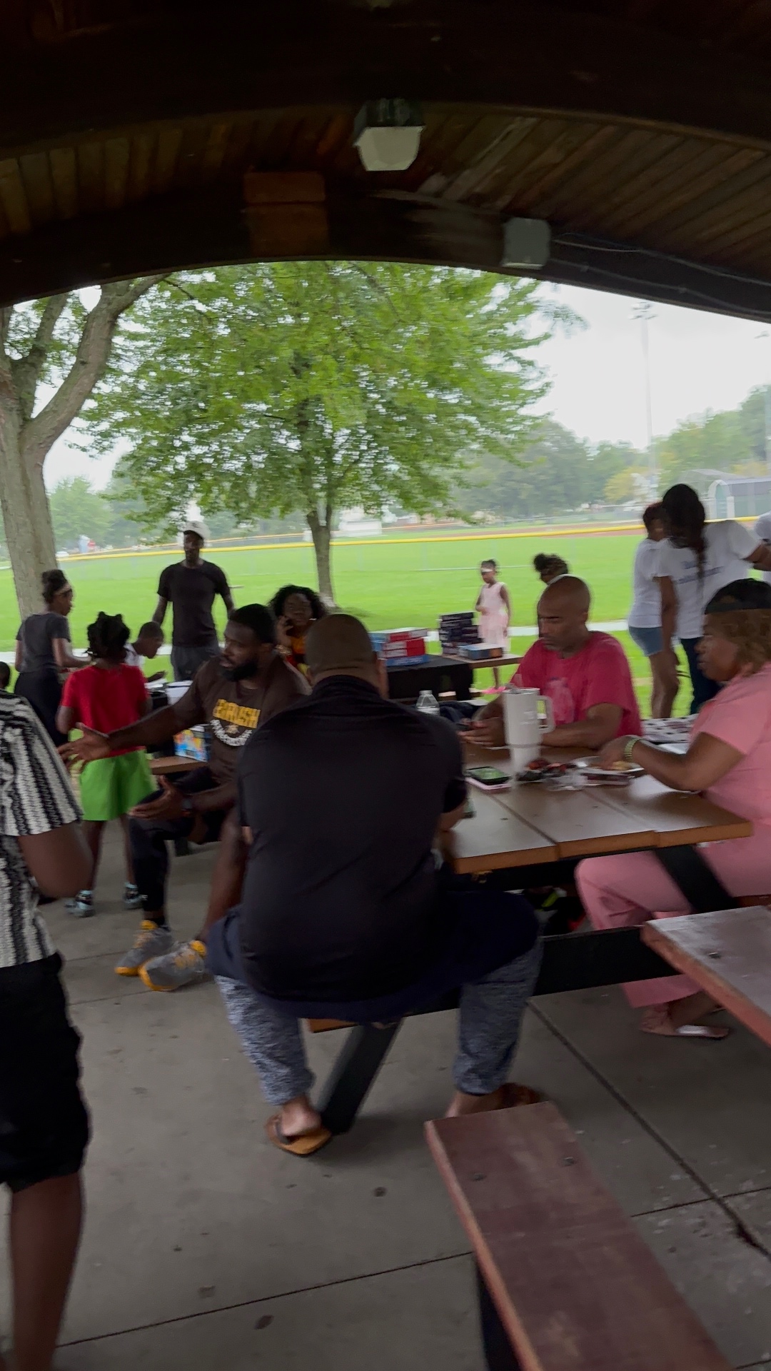 Families gathered at picnic tables under the pavilion with the ballfield in the background at Bexley Park
